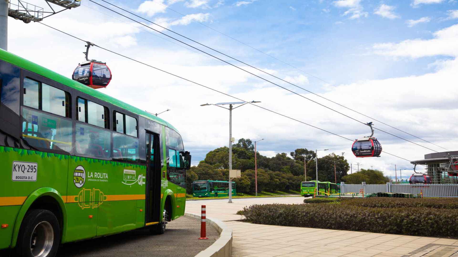 Buses de color verde y teleféricos rojos en una estación de transporte público en Bogotá bajo un cielo nublado