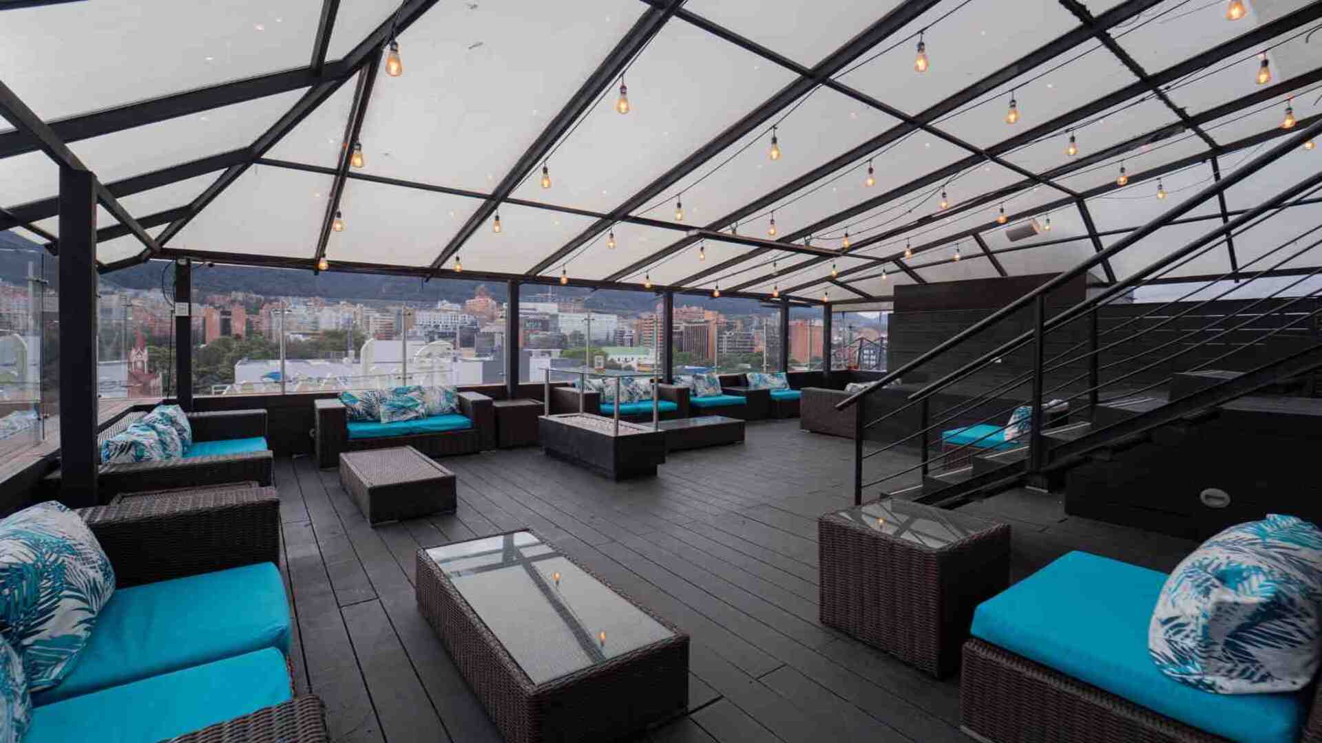 Terraza lounge con vista panorámica de la ciudad, equipada con sofás modernos, mesas y una cubierta iluminada que crea un ambiente elegante y acogedor para el descanso y la socialización.