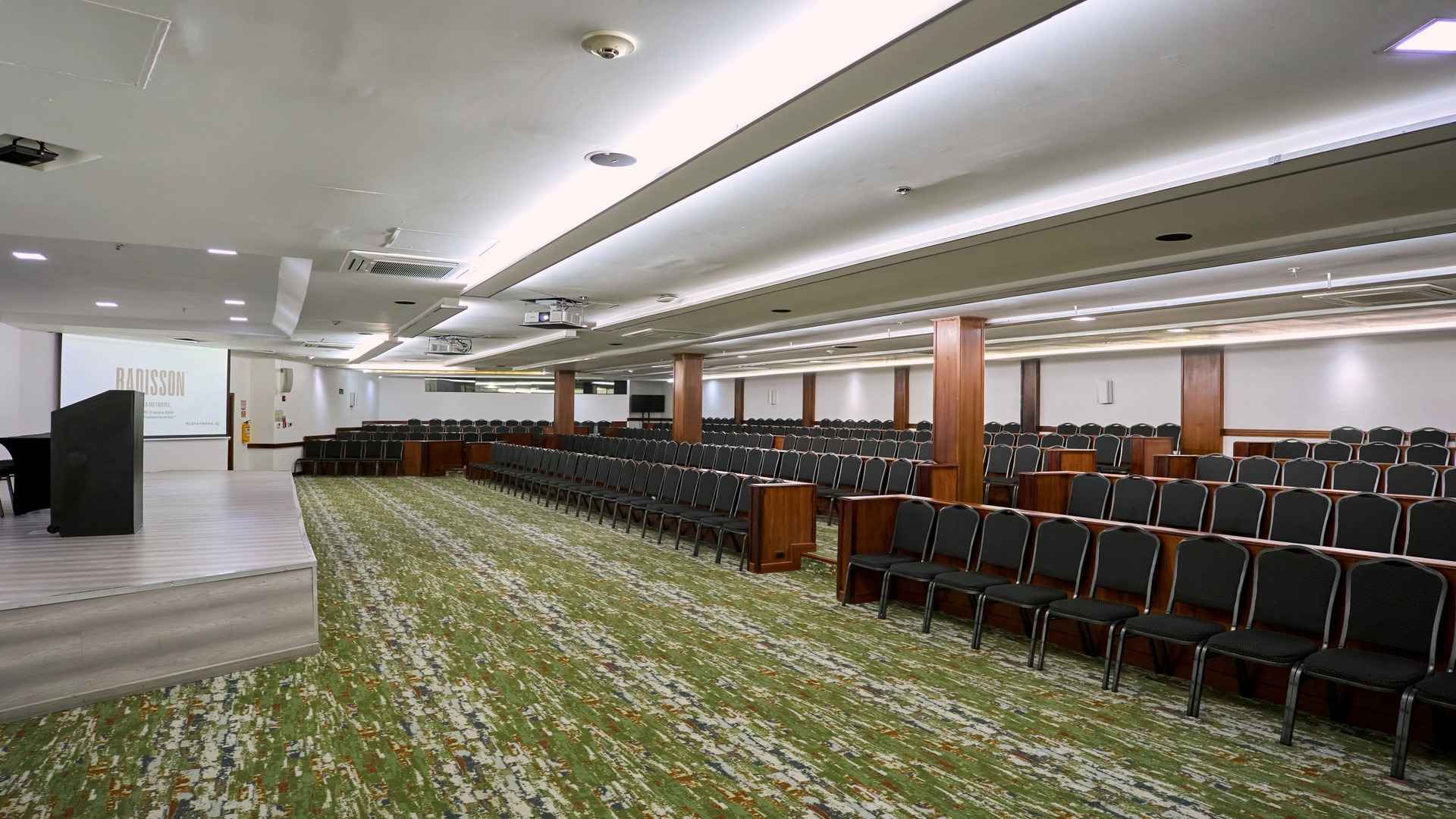 Auditorio amplio y moderno con filas de sillas organizadas frente a un escenario y pantalla de proyección, diseñado para conferencias, eventos corporativos y presentaciones en un ambiente profesional y bien iluminado.