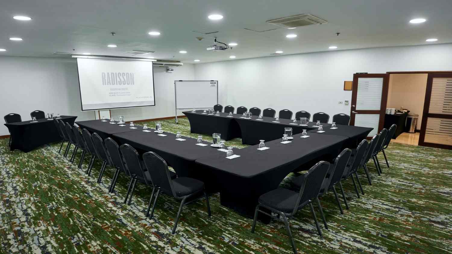 Sala de reuniones corporativa con mesas organizadas en forma de U, equipada con pantalla de proyección, sillas y espacio amplio para capacitaciones, conferencias y encuentros empresariales en un ambiente moderno y funcional.