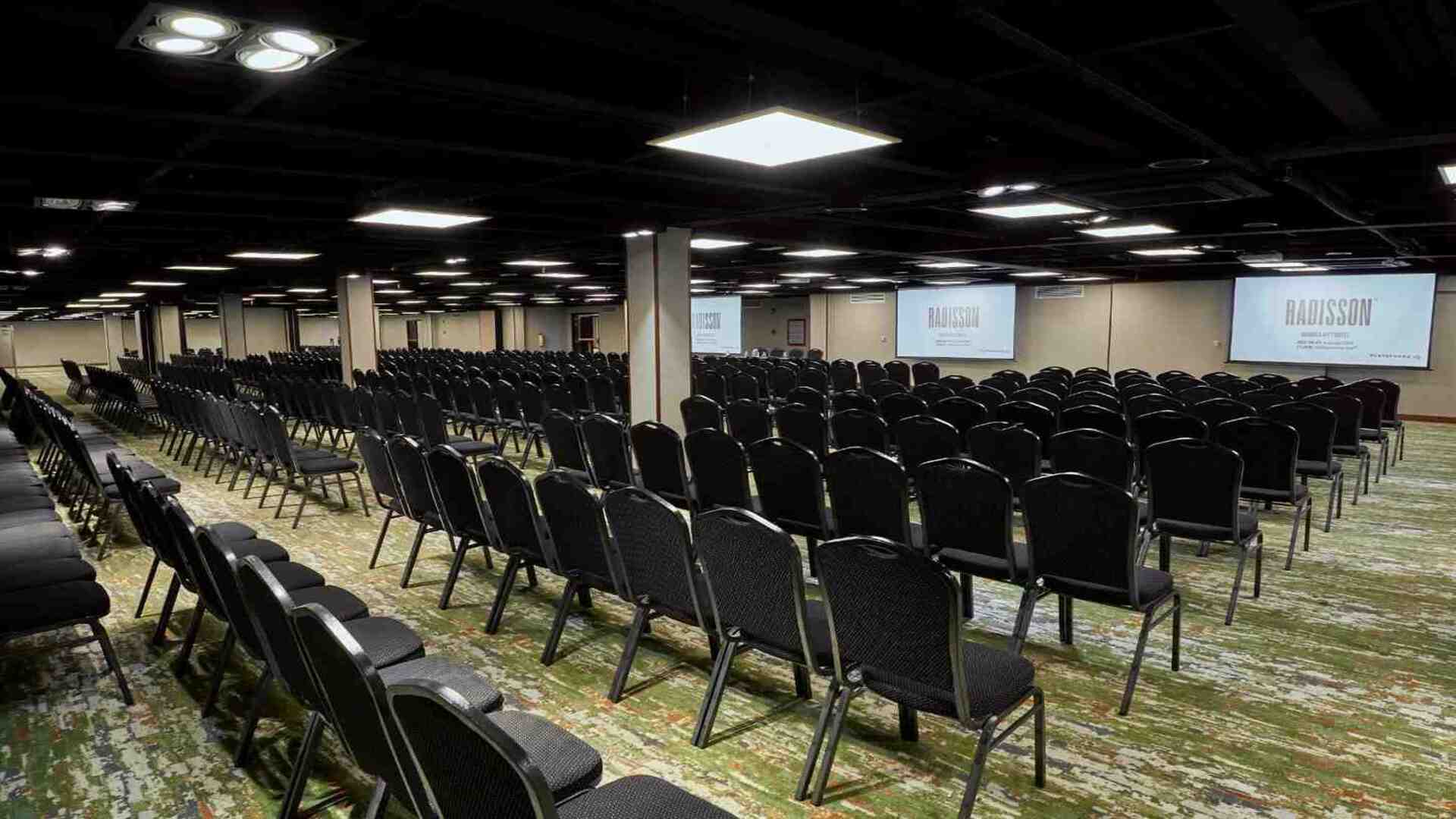 Gran salón para eventos y conferencias con filas de sillas organizadas frente a pantallas de proyección, ideal para congresos, capacitaciones y reuniones corporativas de gran formato.