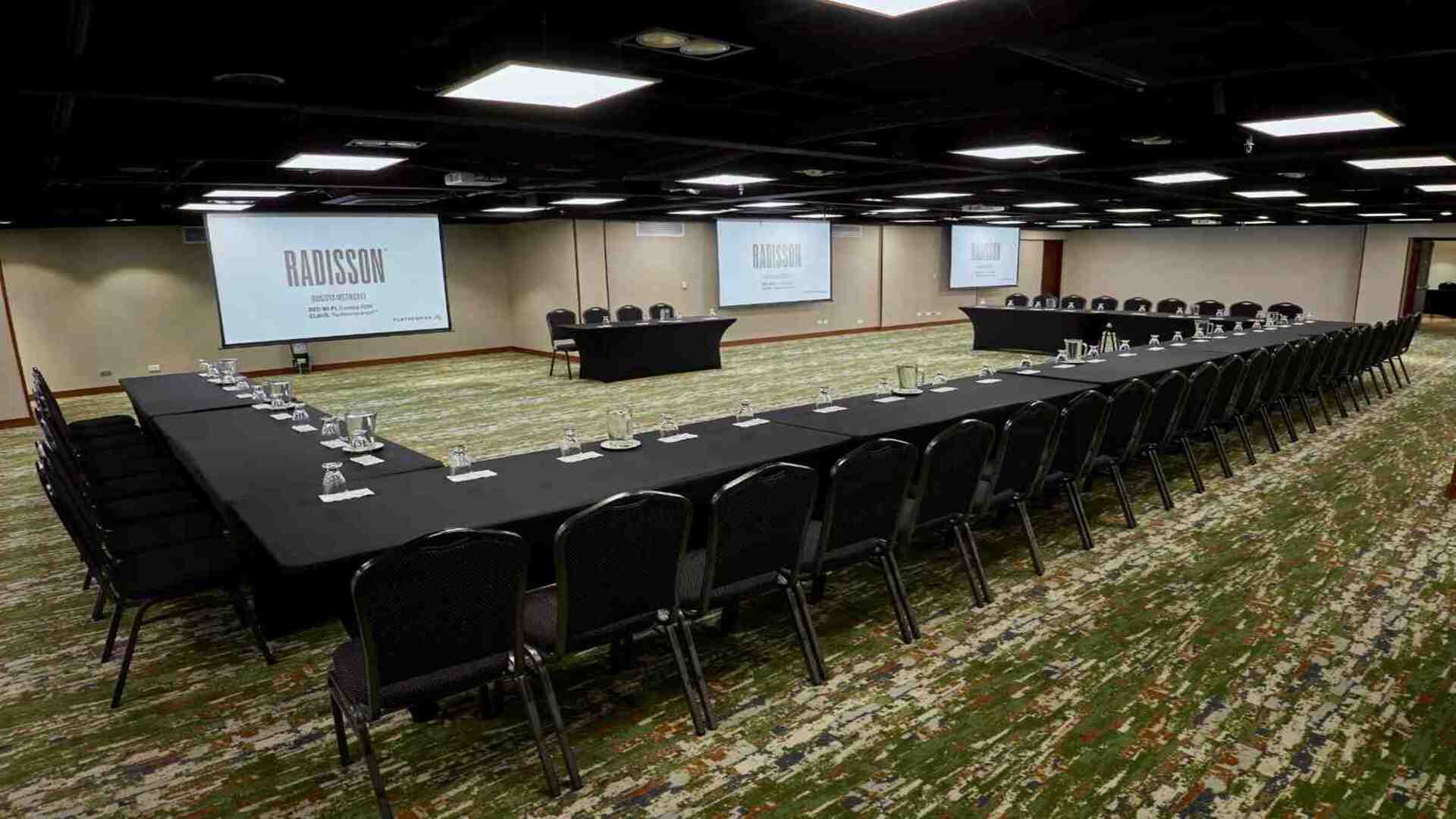 Salón amplio para reuniones y eventos corporativos con montaje tipo U, pantallas de proyección y espacio ideal para conferencias y capacitaciones.