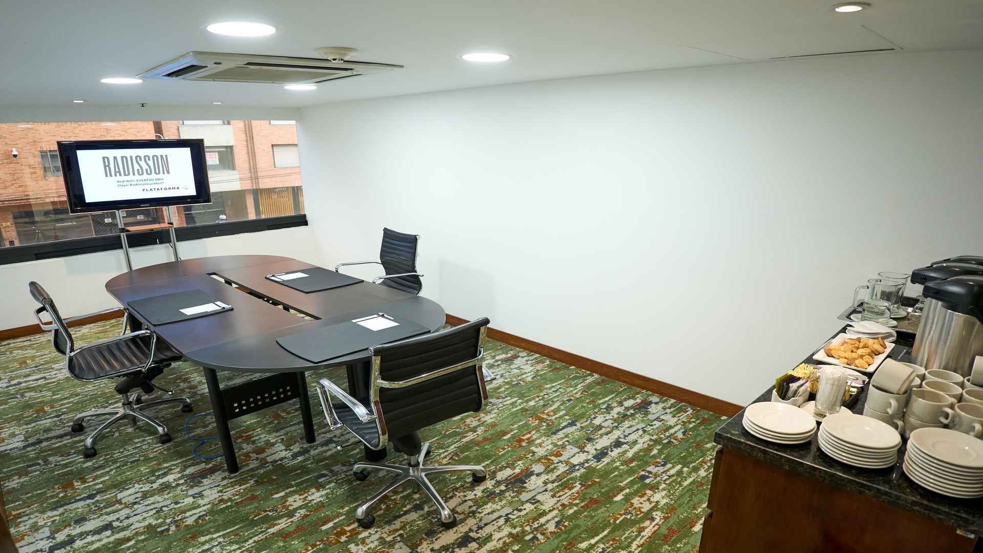 Sala de juntas moderna con mesa ovalada, sillas ejecutivas y estación de café, ideal para reuniones corporativas privadas.