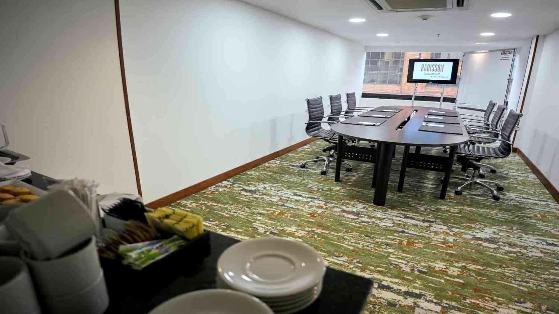 Sala de juntas ejecutiva con mesa central, sillas ergonómicas y estación de café, ideal para reuniones empresariales privadas.