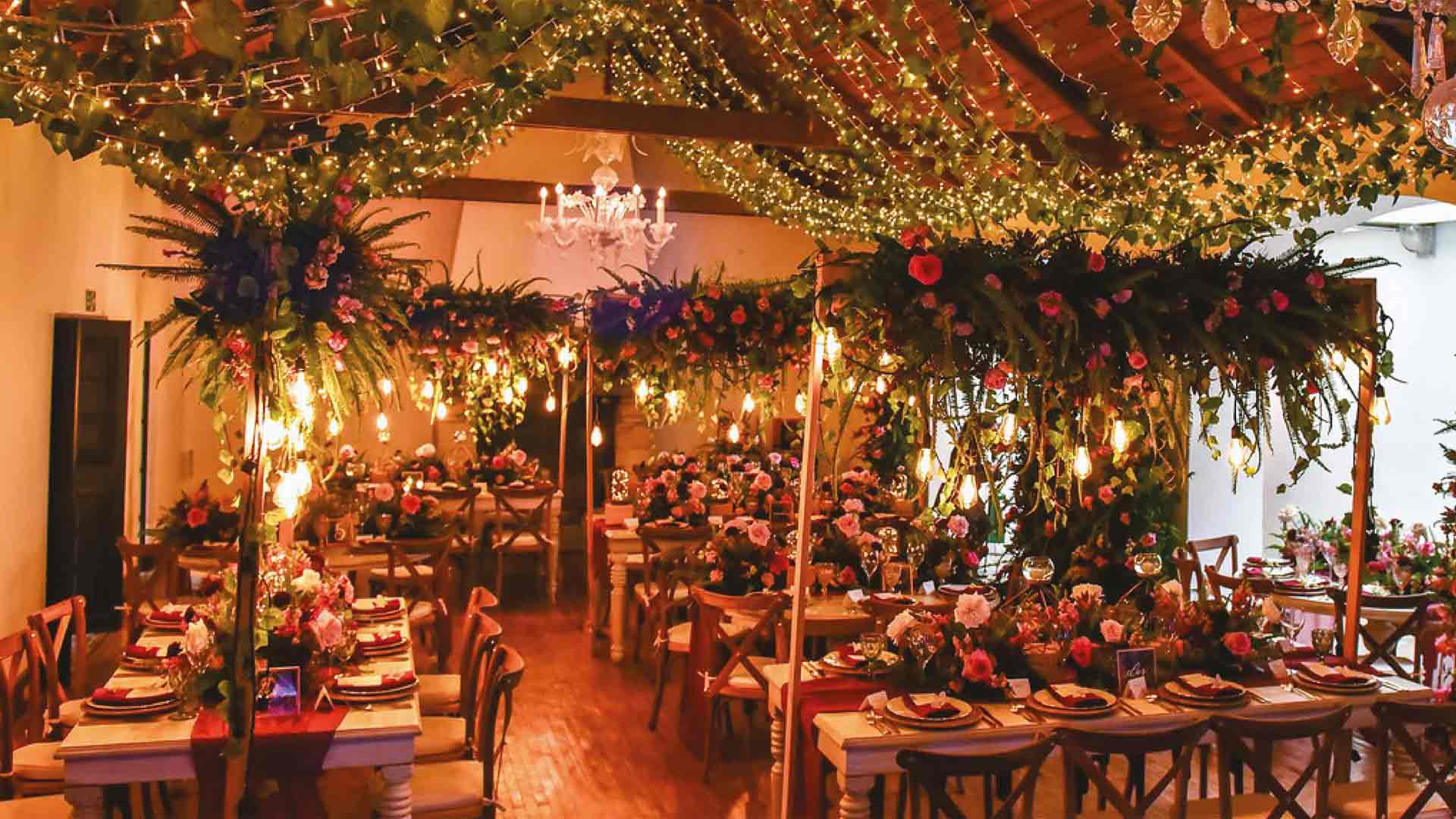 Un elegante salón del Museo El Chicó está decorado con exuberantes arreglos florales, guirnaldas de luces y mesas cuidadosamente ambientadas. La iluminación cálida y el entorno colonial crean un ambiente sofisticado e íntimo, ideal para la realización de eventos especiales.