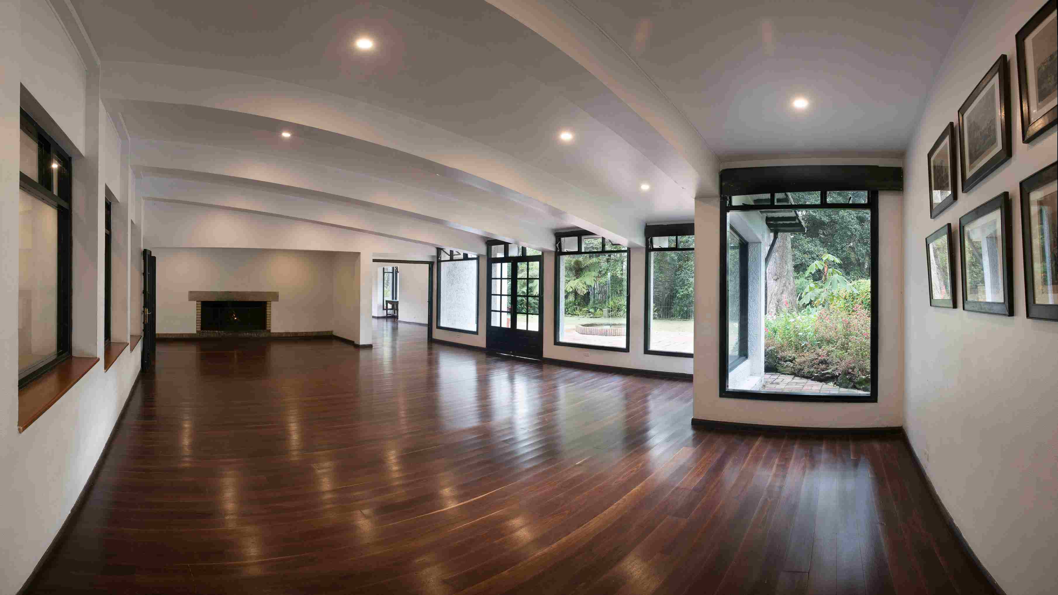 Un amplio salón de diseño contemporáneo destaca por sus pisos de madera, grandes ventanales con vista al jardín y una acogedora chimenea. Su ambiente luminoso y elegante lo convierte en un espacio ideal para eventos sociales, reuniones y actividades culturales.