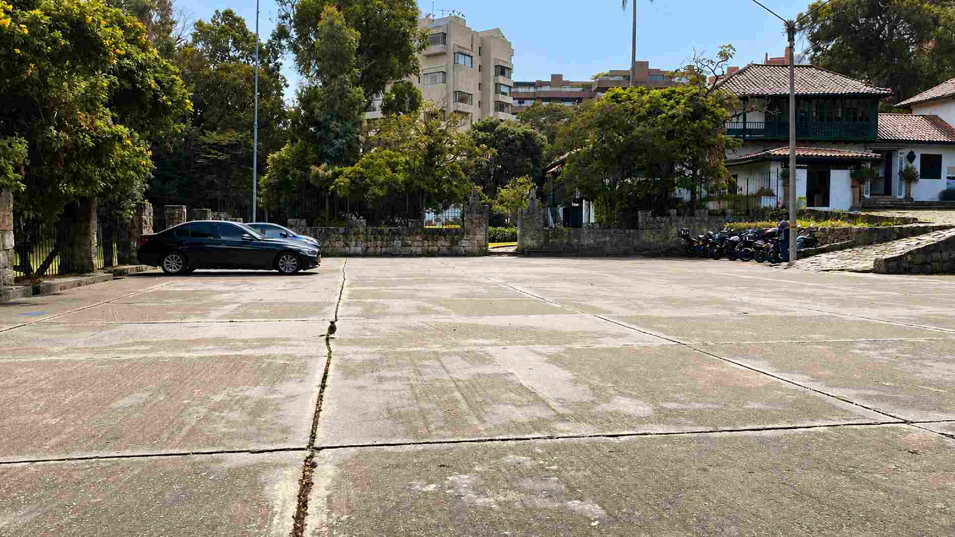 Una amplia zona de estacionamiento se encuentra frente a una casona de arquitectura colonial, rodeada de árboles y jardines. El espacio ofrece un acceso cómodo y seguro para visitantes, en un entorno que combina patrimonio histórico y naturaleza.