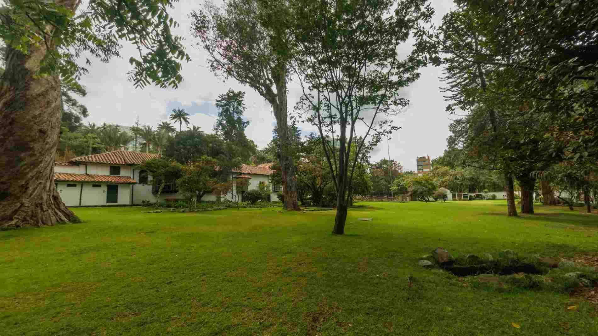 Un extenso jardín rodeado de árboles centenarios y amplias zonas verdes enmarca una casona de arquitectura colonial con techos de teja. Este entorno natural ofrece un ambiente tranquilo y acogedor, ideal para disfrutar del patrimonio y la naturaleza en Bogotá.