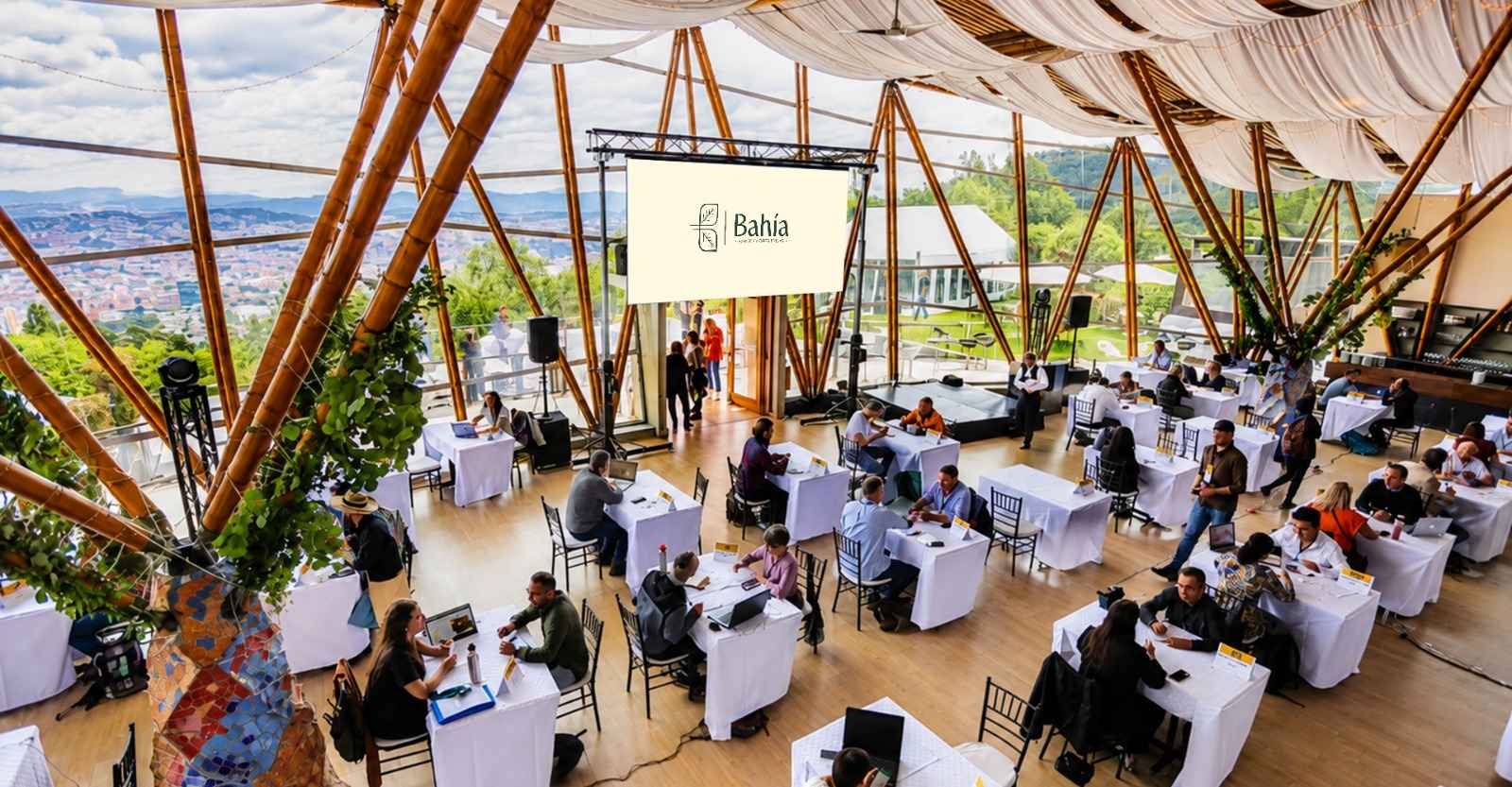 Un moderno y luminoso espacio para eventos, rodeado de grandes ventanales que ofrecen una espectacular vista de la ciudad y las montañas. Las mesas dispuestas para reuniones y la arquitectura en bambú crean un ambiente elegante, natural y versátil para encuentros corporativos y celebraciones.
