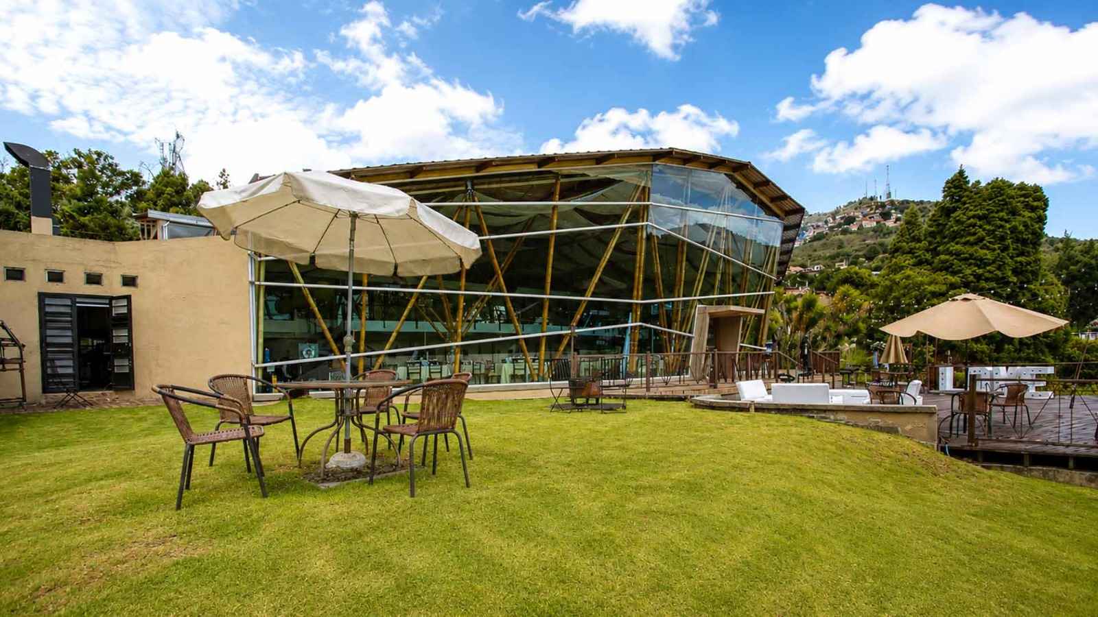 Una amplia terraza de madera se abre hacia un paisaje natural, creando un escenario elegante y luminoso para eventos al aire libre. El mobiliario blanco, la iluminación decorativa y la espectacular vista de las montañas aportan un ambiente sofisticado, relajado y especial.