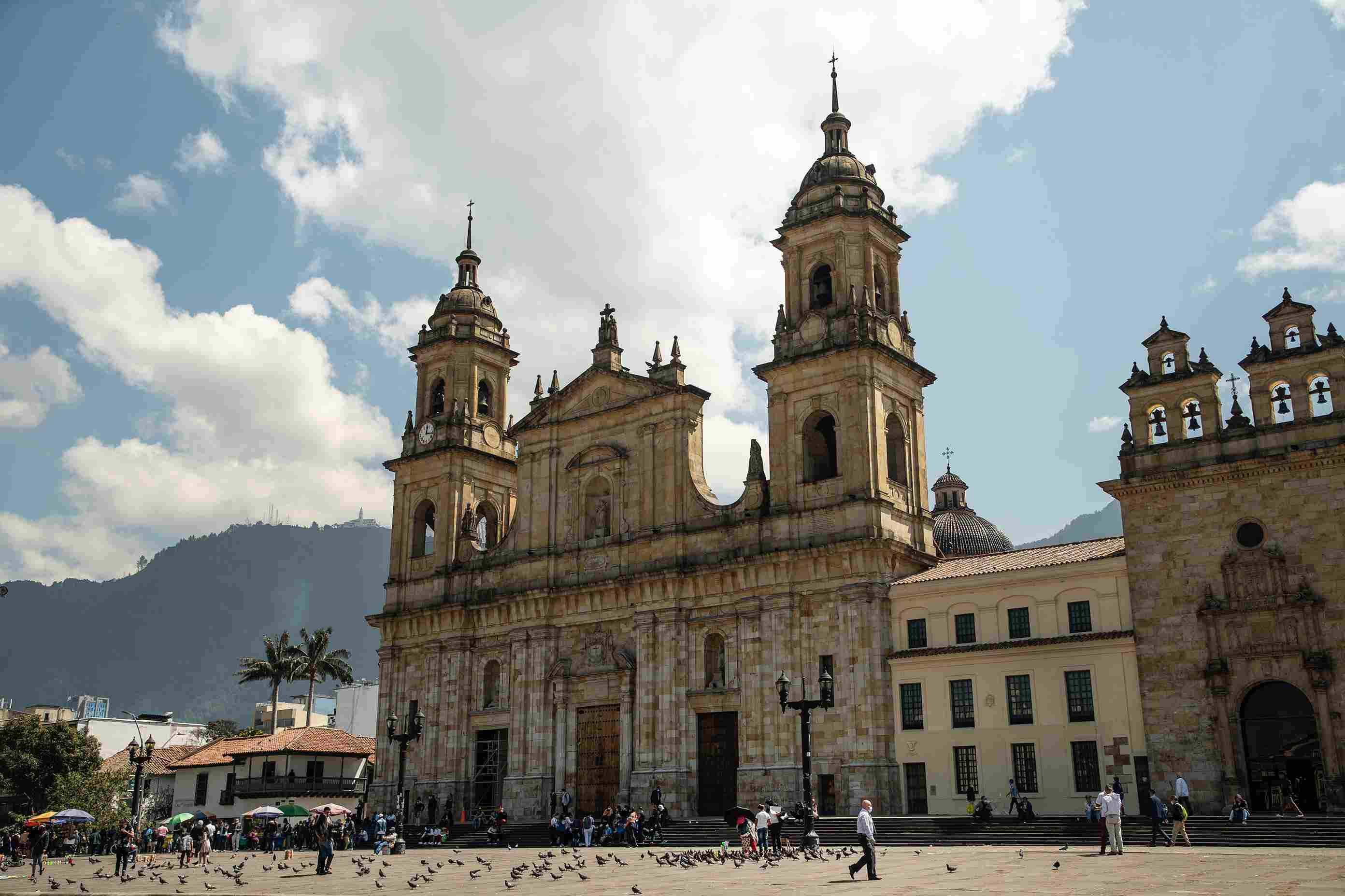 Catedral Primada de Colombia en la Plaza de Bolívar, rodeada de visitantes, arquitectura histórica y las montañas de Bogotá.