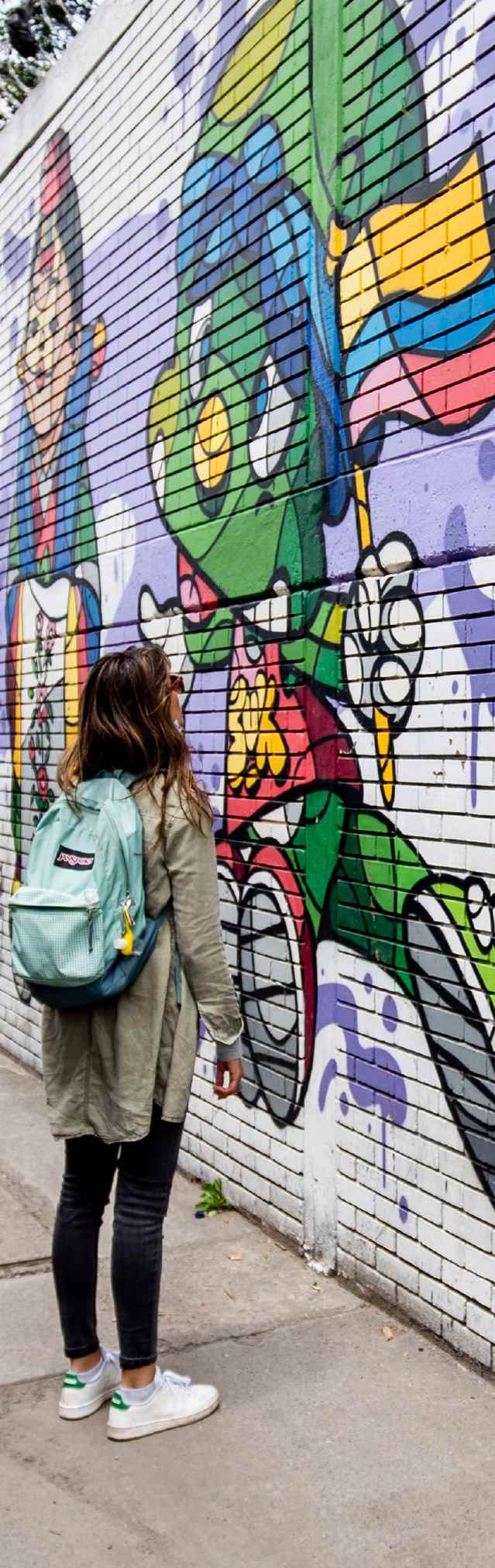 Visitante contempla un colorido mural de arte urbano en una calle de Bogotá.