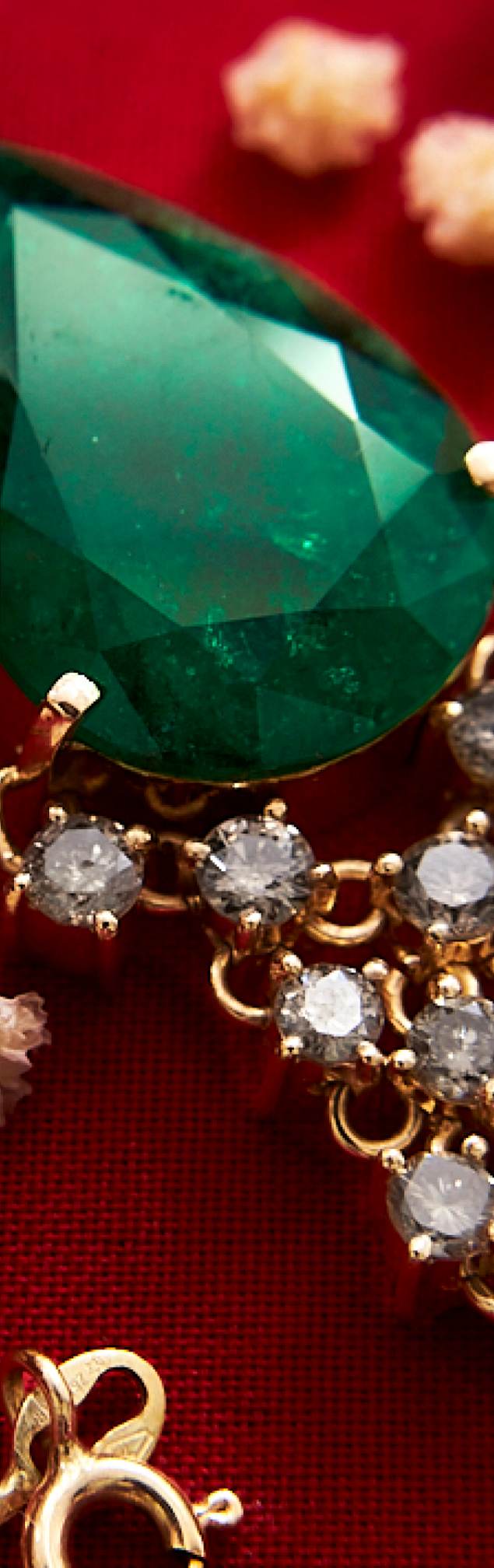 Primer plano de una joya en oro con una gran esmeralda colombiana y piedras preciosas, sobre un fondo rojo.