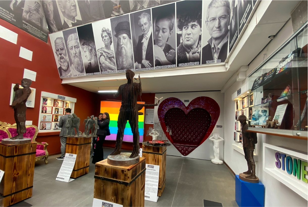 Salón del Museo LGBTI al interior con esculturas y fotografías, y la presencia de 2 mujeres y un hombre.