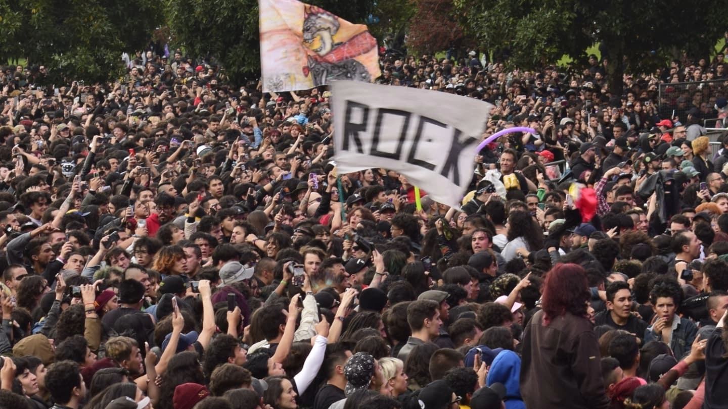 Multitud de asistentes disfruta de un concierto de rock al aire libre, con las manos levantadas y banderas en medio del público.