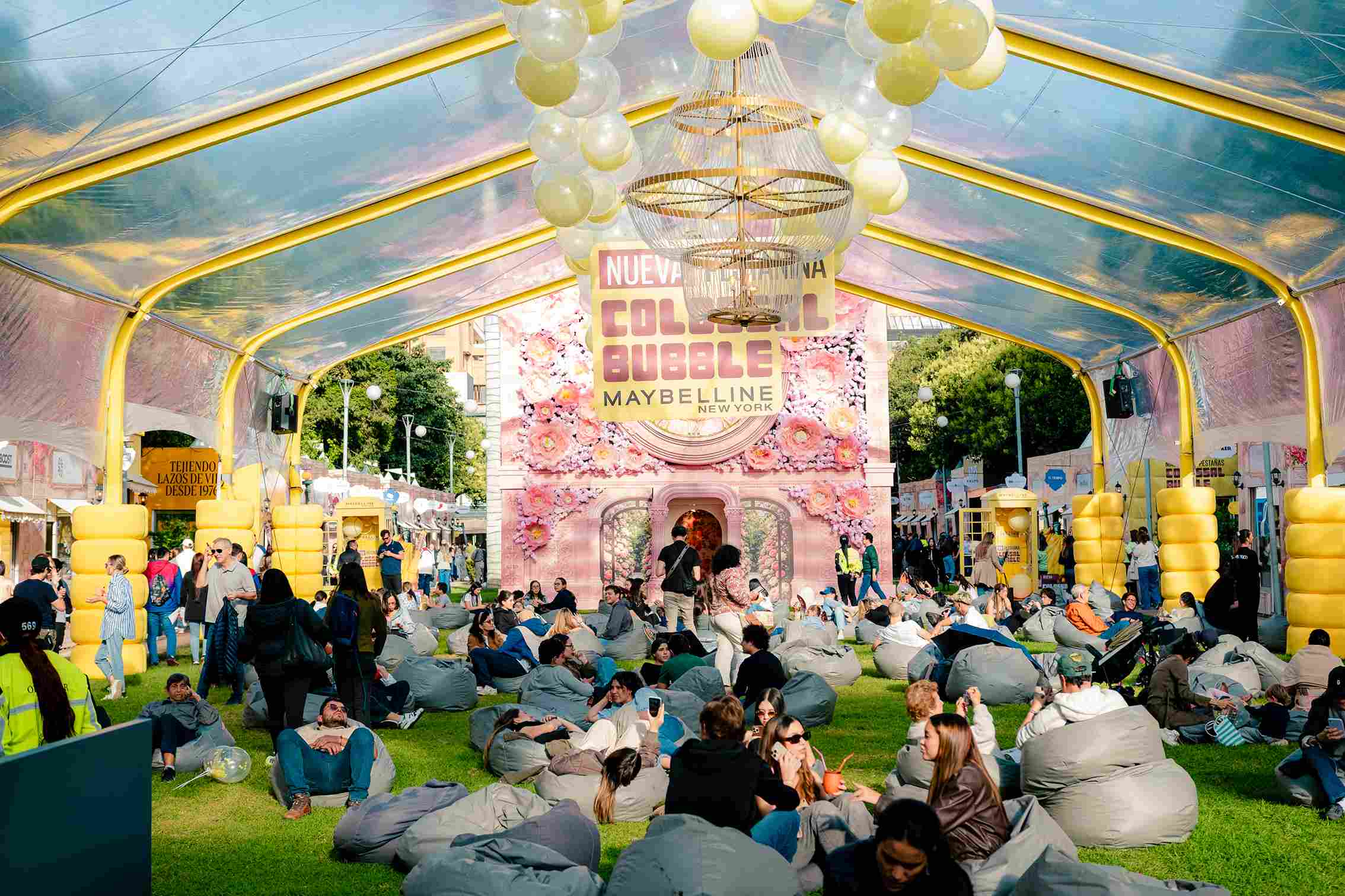 Un público disfruta de una activación al aire libre, con zonas de descanso, globos y una colorida instalación de Maybelline.