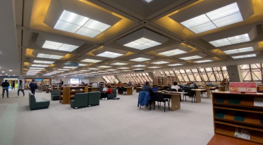 Biblioteca Luis Ángel Arango interior con ventanales en techo y paredes. Se observa personas sentadas al rededor de mesas