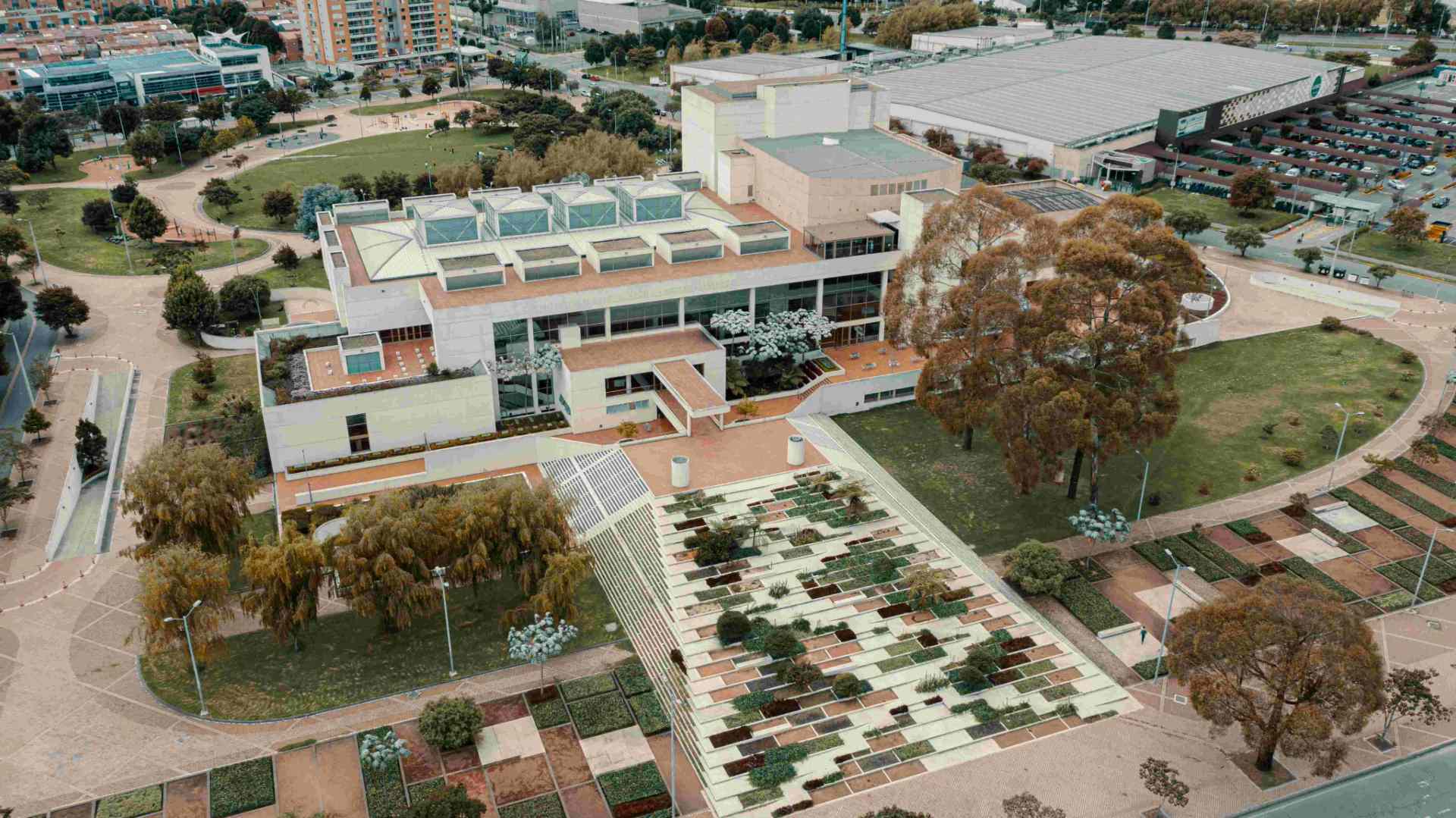 Biblioteca Julio Mario Santo Domingo desde arriba de día en dron edificio blanco rodeado de zonas verdes, árboles, parqueadero y barrio aledaño.