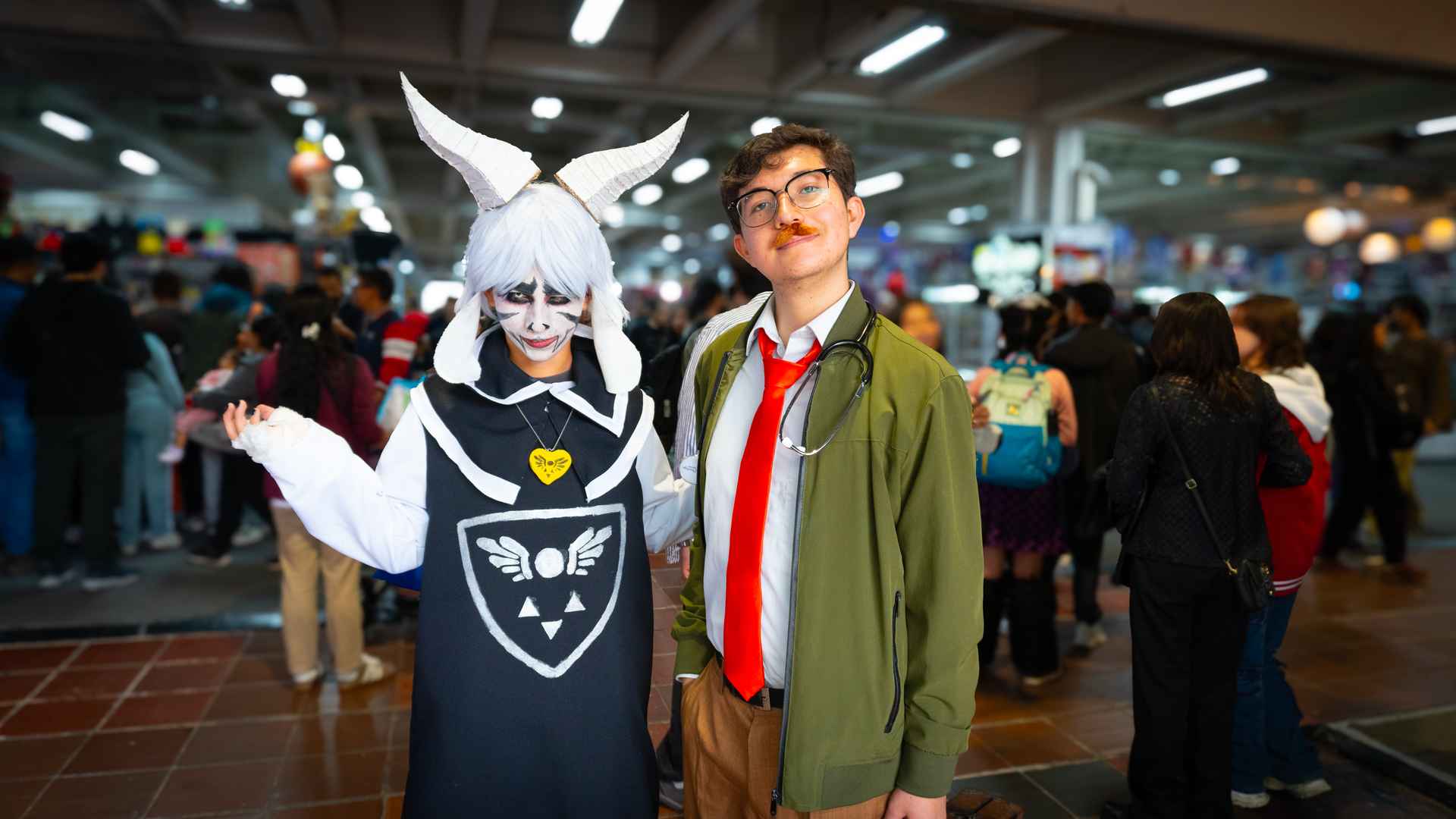 Dos jóvenes posan con disfraces y pelucas de personajes de fantasía en un festival cultural.