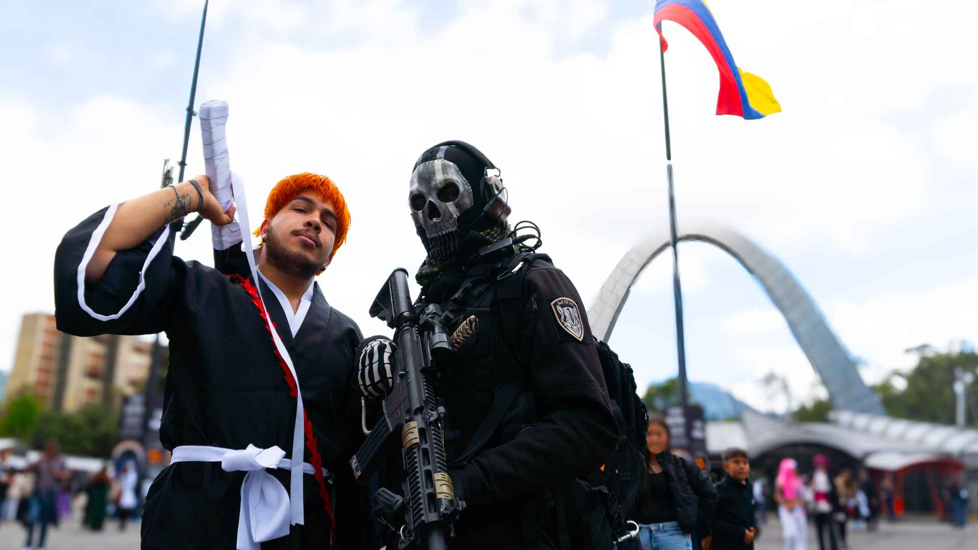 Dos jóvenes con disfraces y accesorios posan en la plaza de Corferias bajo un cielo nublado.