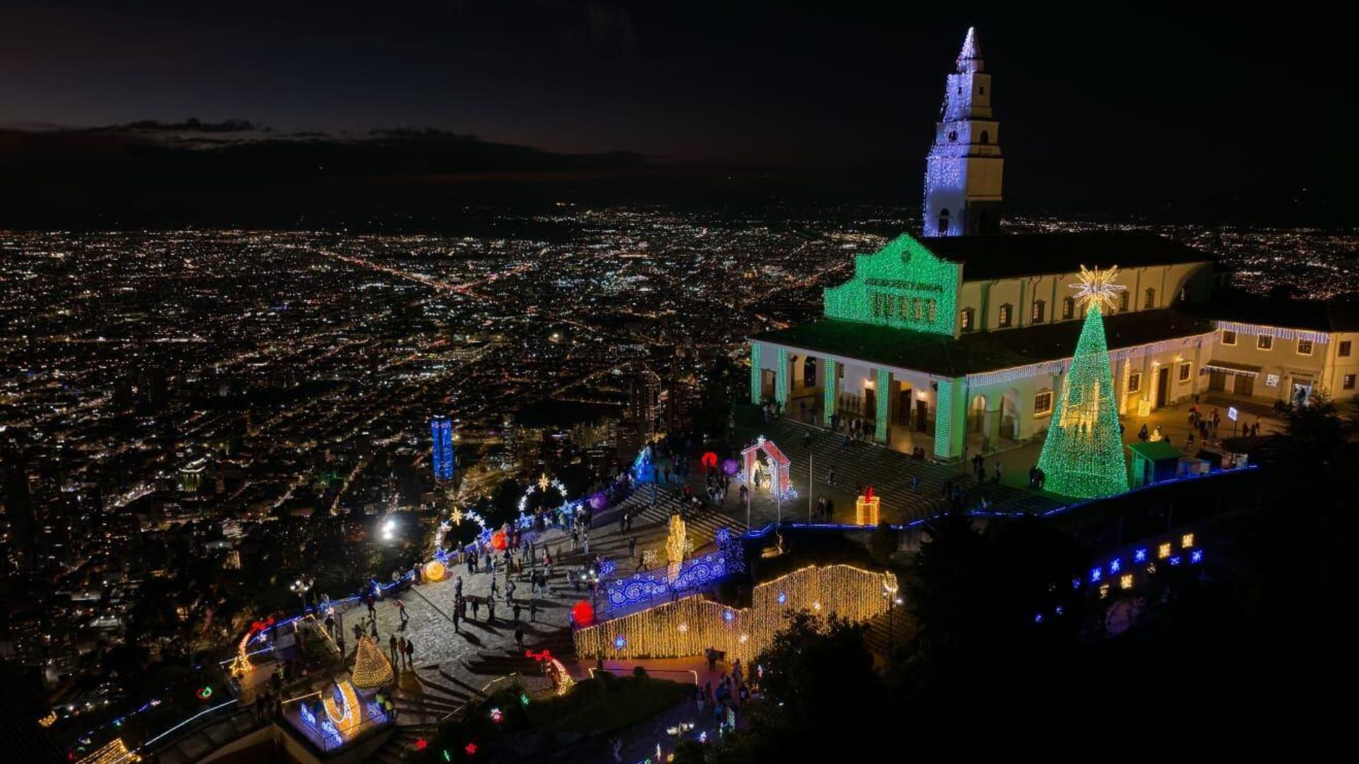 Santuario de Monserrate iluminado de verde sobre la panorámica nocturna de la ciudad llena de luces.