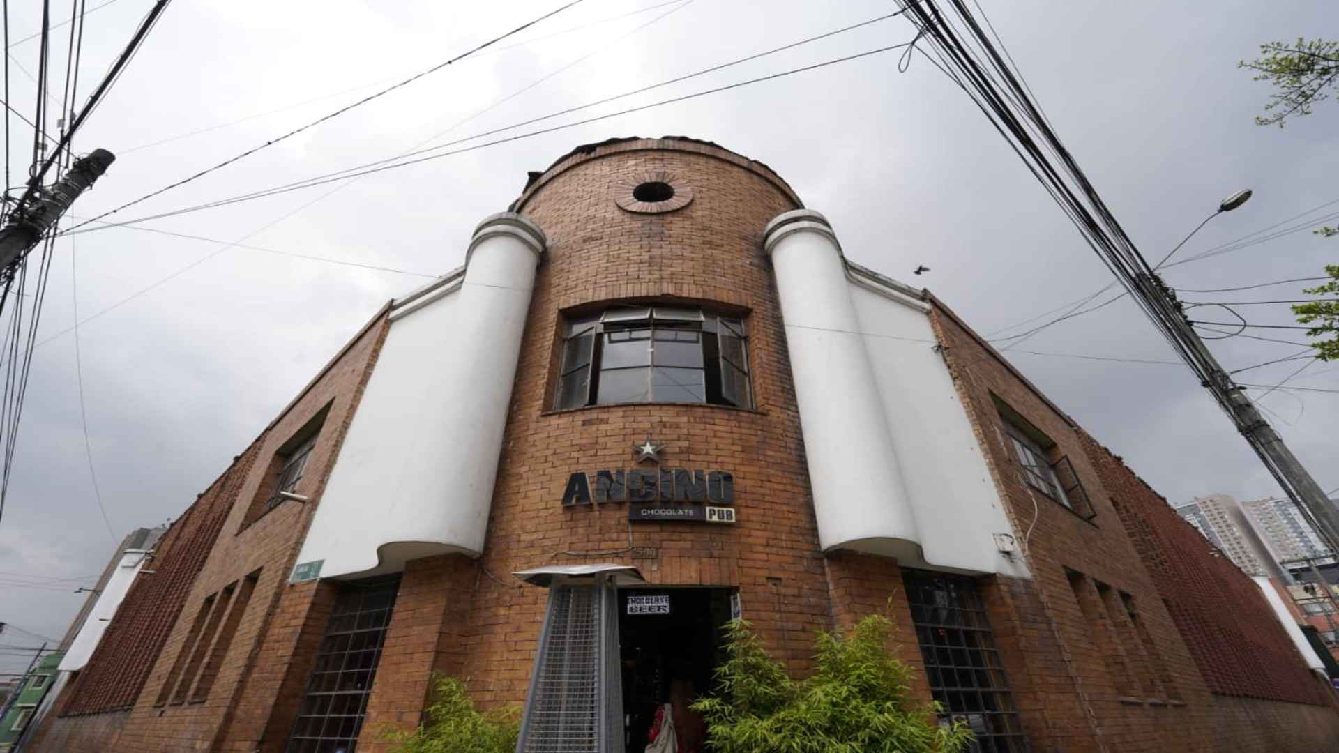 Fachada de ladrillo de Andino Chocolate Pub. Estructura simétrica de estilo industrial con columnas blancas y cables.