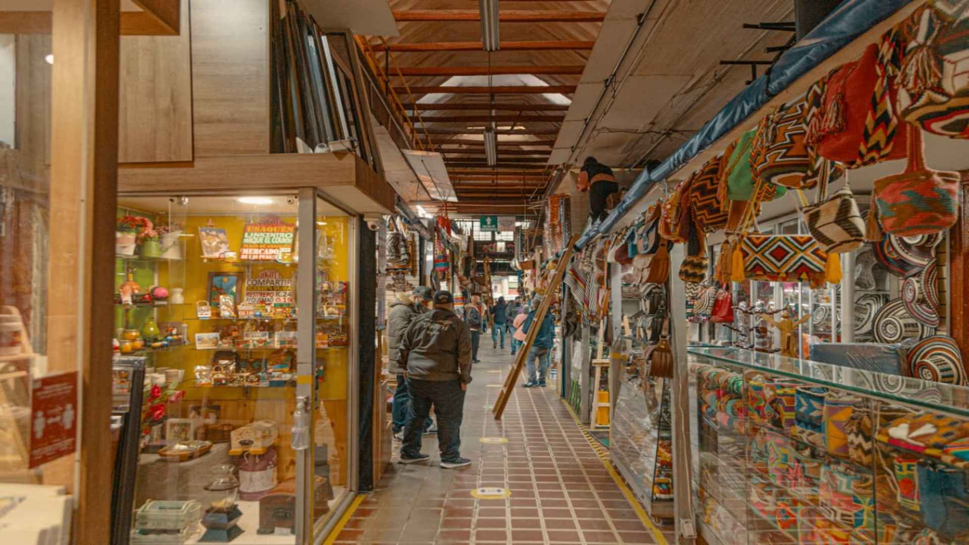Pasillo histórico del tradicional Pasaje Rivas lleno de coloridas mochilas y artesanías típicas que representan la cultura popular bogotana.