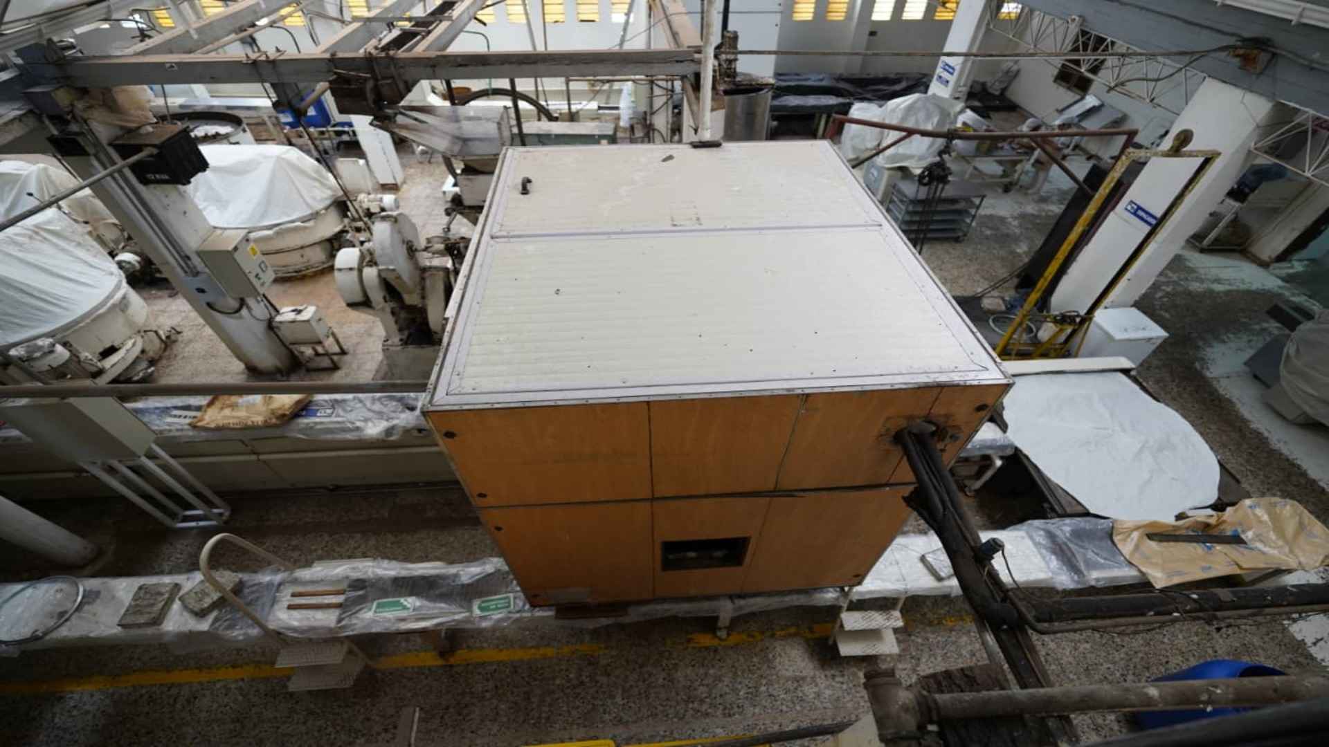 Vista aérea de maquinaria de fábrica con una gran caja central de madera, tubos conductores y equipo industrial.