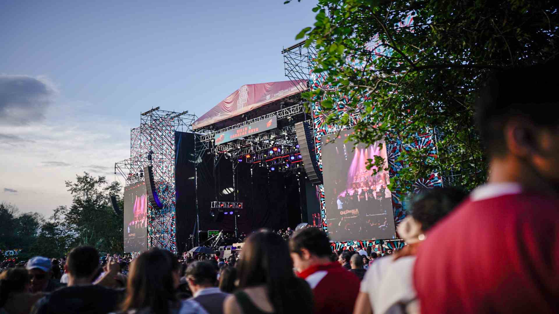 Una multitud disfruta frente al gran escenario al aire libre, rodeado de la naturaleza y energía del Parque de los Novios.