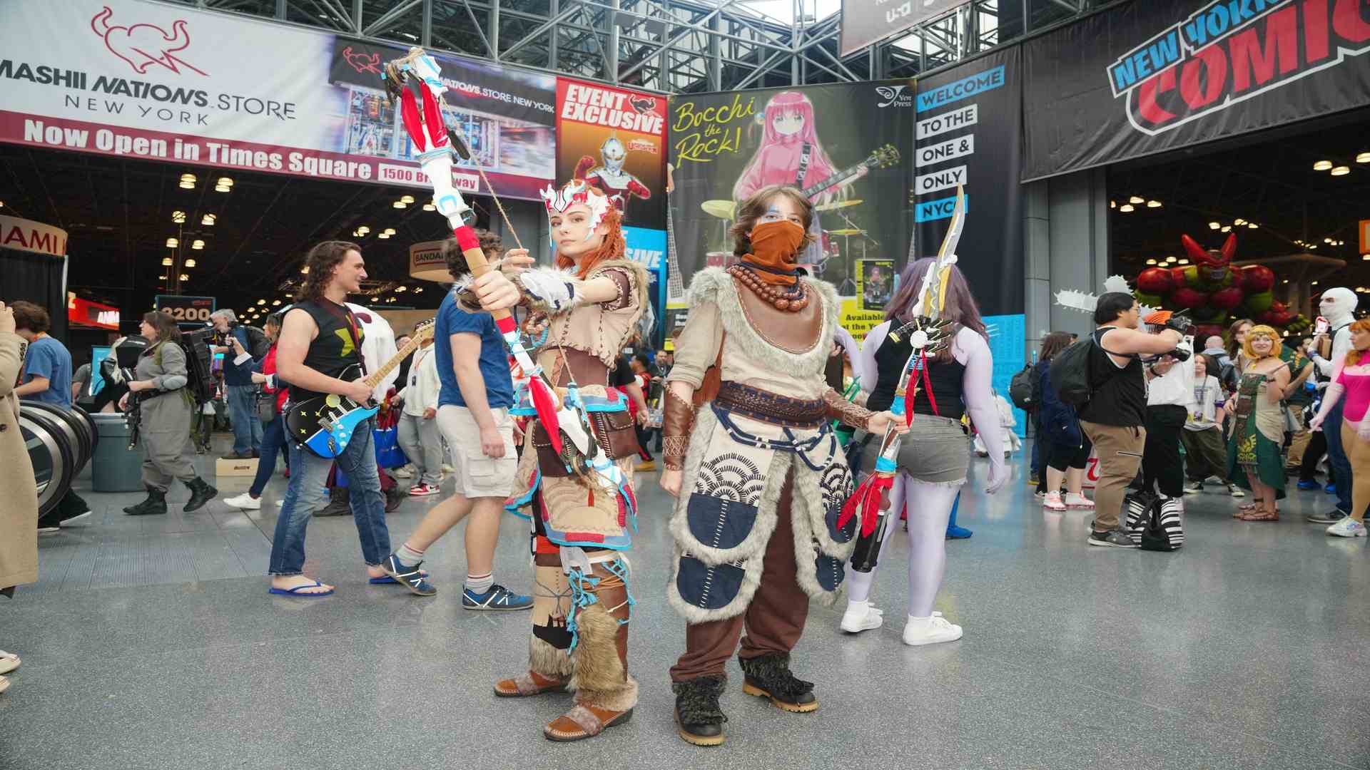 Dos personas vestidas con detallados cosplays de guerreros sostienen armas artesanales en medio de una convención.