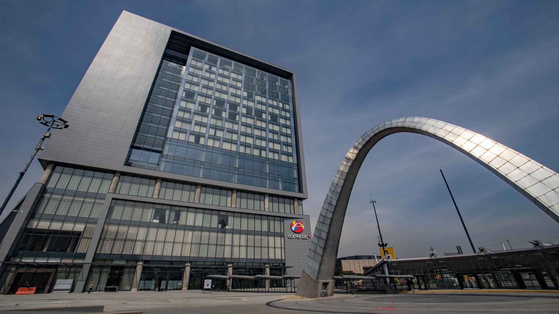 Vista exterior de la fachada moderna y el acceso peatonal de Corferias bajo un cielo despejado. 