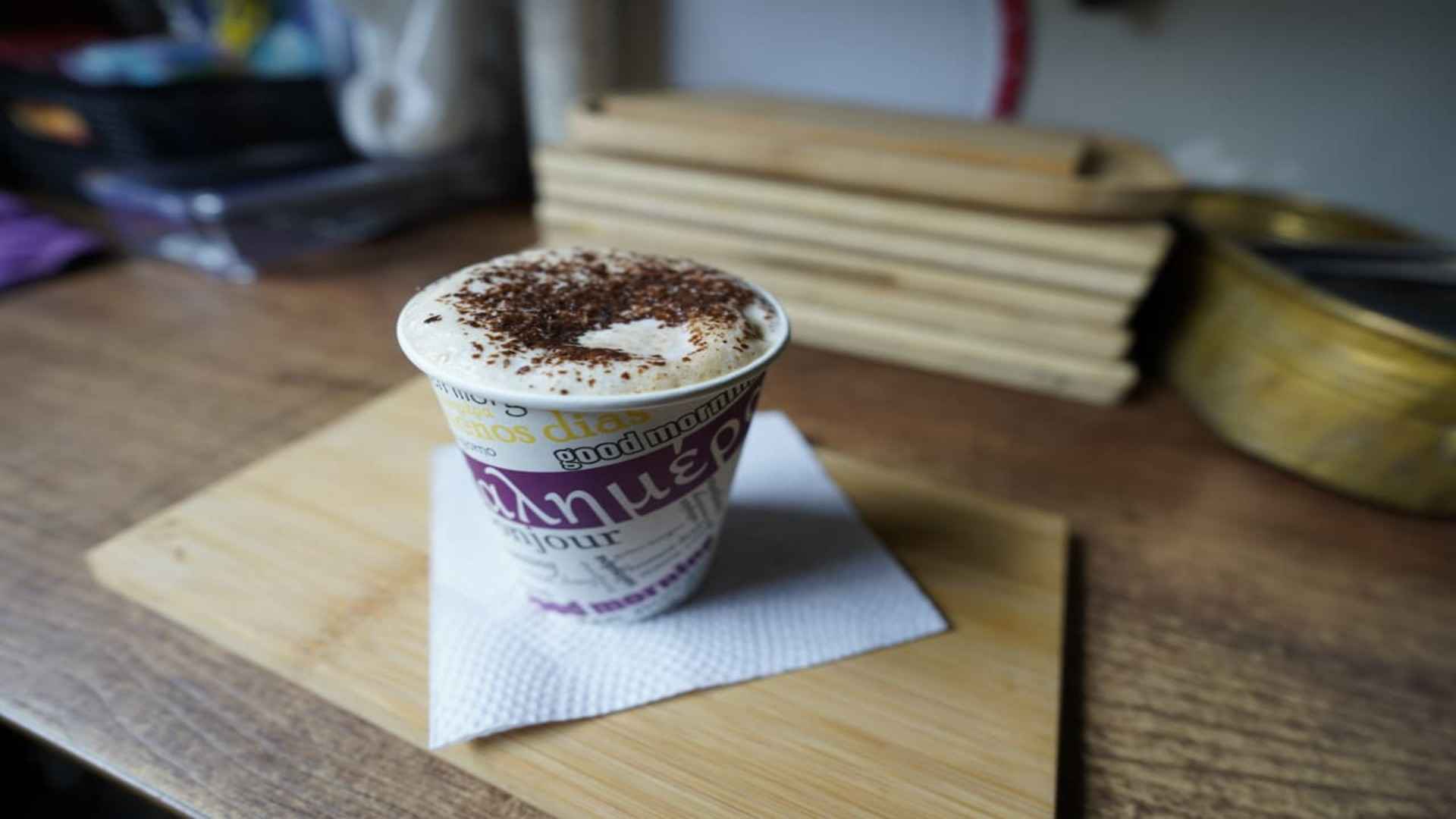 Vaso de chocolate con espuma y canela en polvo sobre servilleta y tabla de madera en un mostrador borroso.
