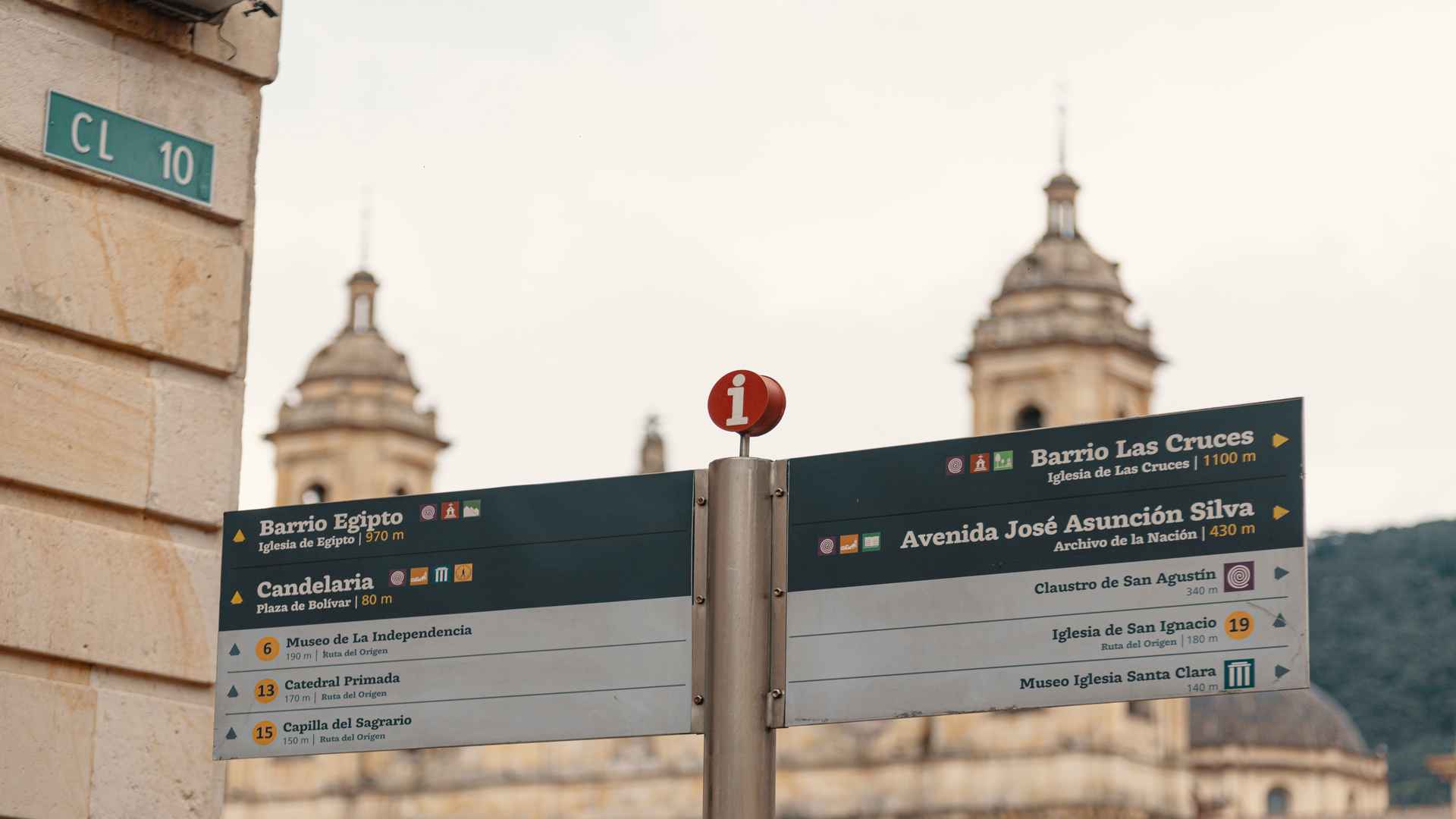 Letreros turísticos e informativos con direcciones históricas, con las cúpulas de la Catedral Primada al fondo.