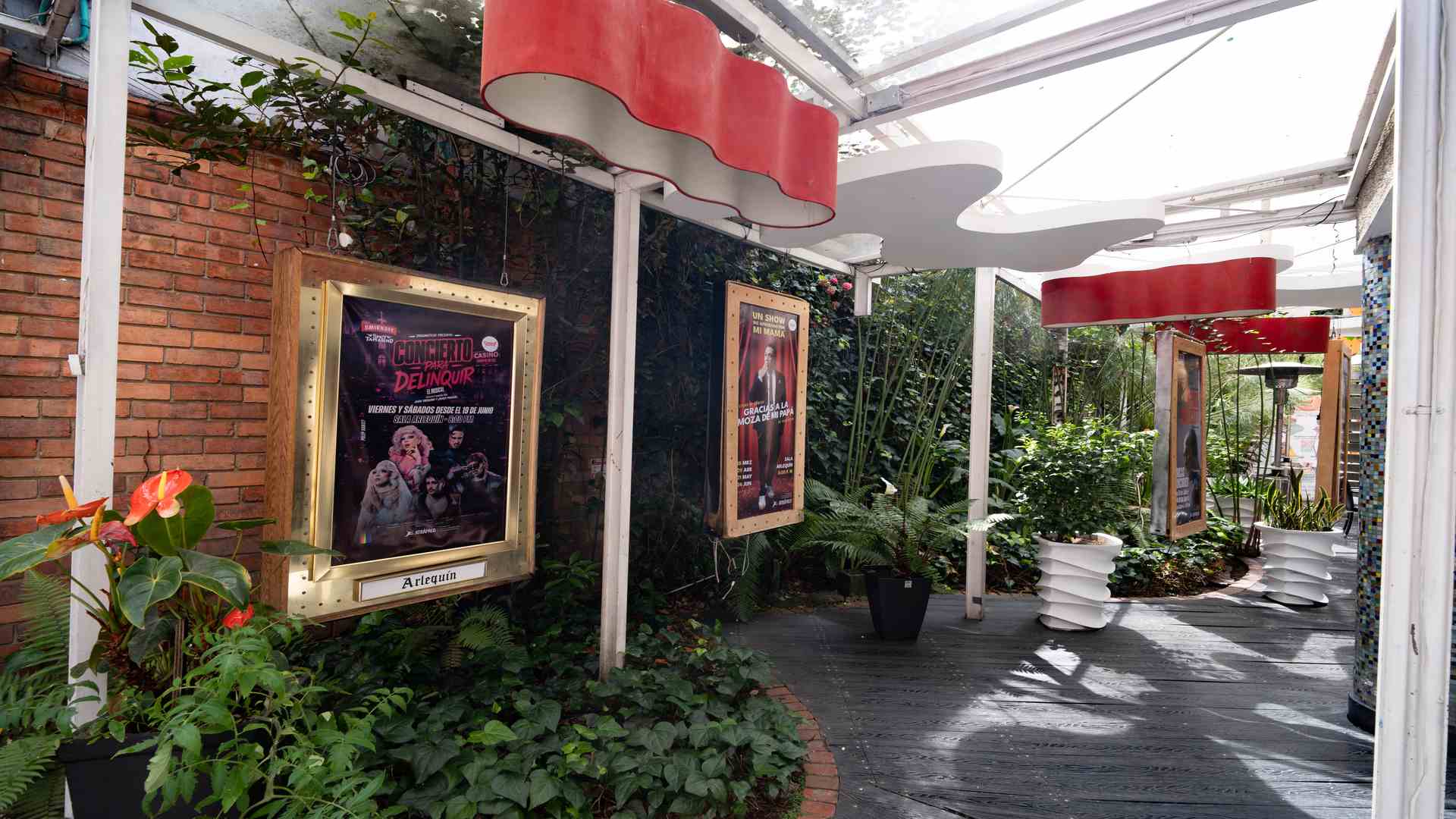 Pasillo con marquesinas e iluminadas con afiches promocionales de las obras de teatro, rodeado de plantas y flores.
