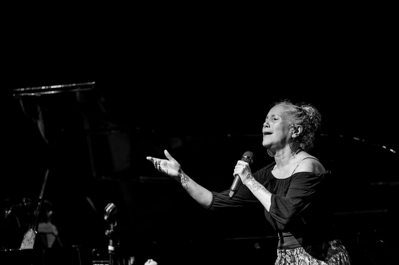 Una cantante interpreta una canción sobre el escenario, micrófono en mano y con el brazo extendido hacia el público. La fotografía en blanco y negro resalta la intensidad y emotividad del momento.
