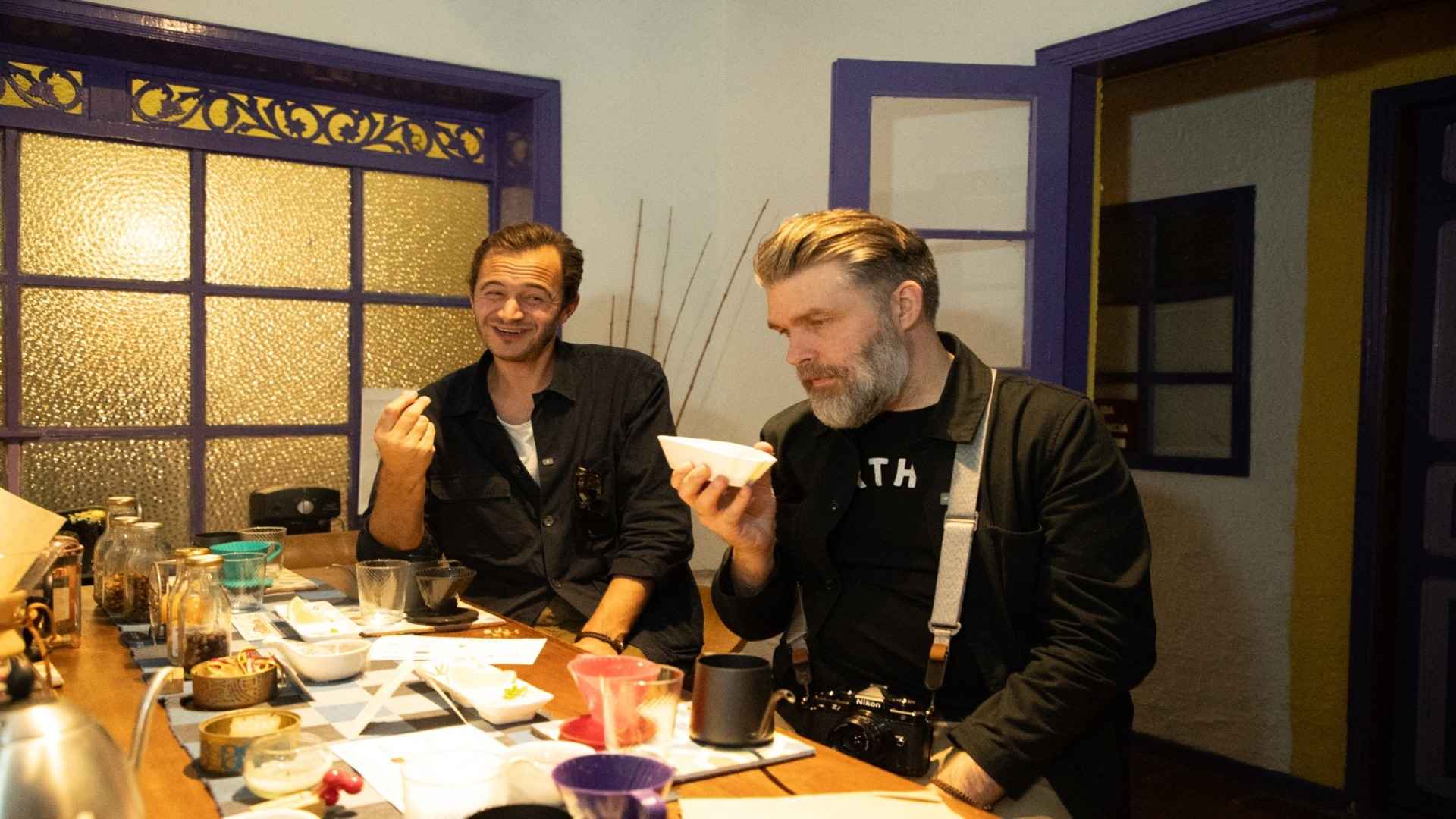 Dos hombres sentados a la mesa observan y prueban con atención tazas de café en una tienda especializada.