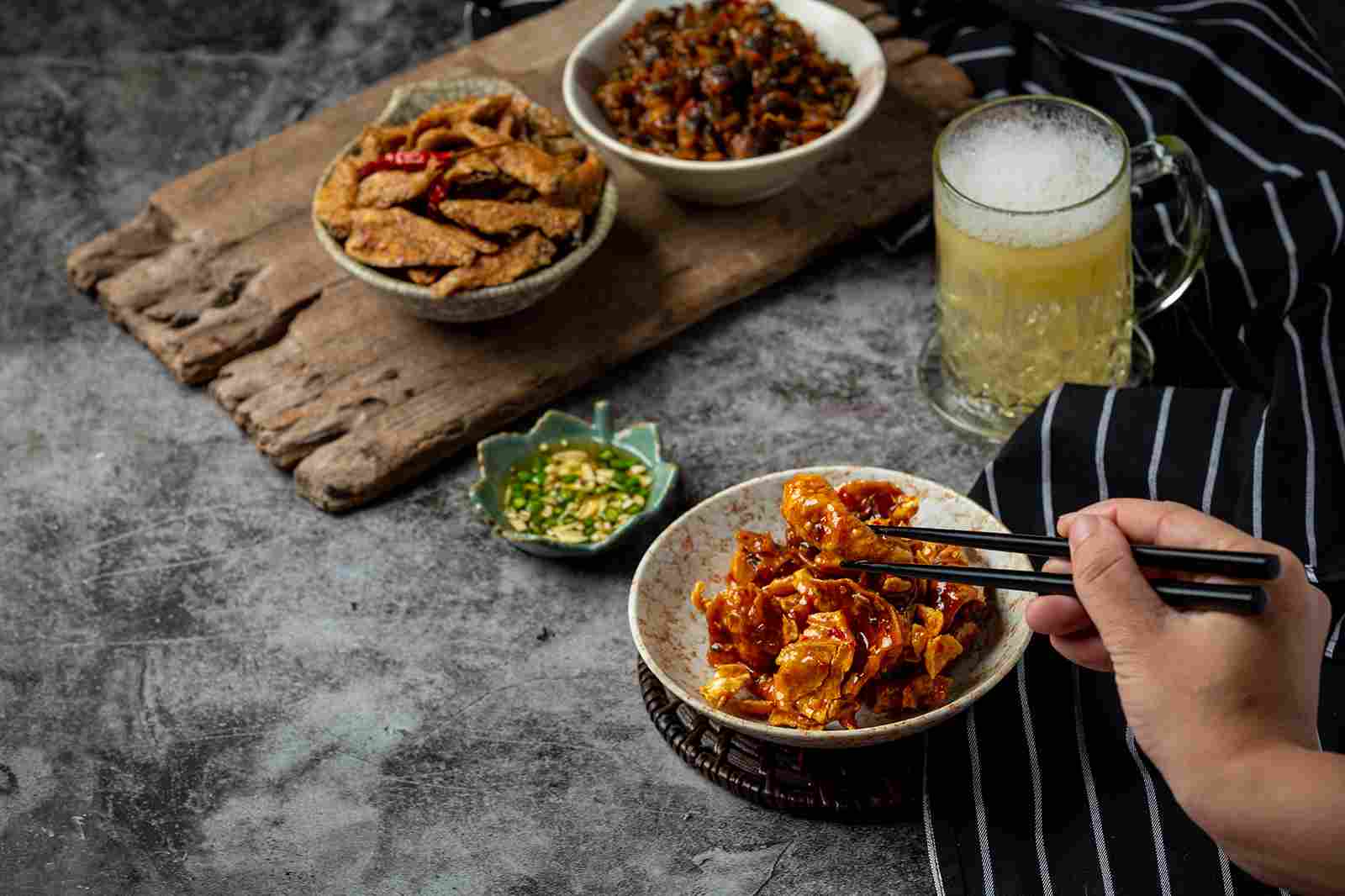 Platos de comida coreana acompañados de vegetales y salsas, servidos junto a una bebida fría y disfrutados con palillos.