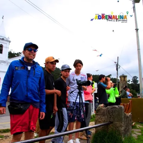 Grupo de personas jóvenes junto con un guía hombre, observando un mirador. Todos con ropa deportiva, algunos hombres llevan gorra, otros binoculos.