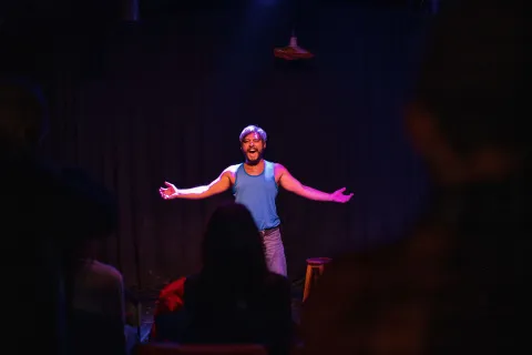 Barraca Teatro con artista hombre joven en tarima sonriendo ante un público.