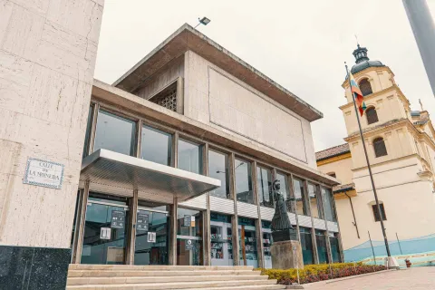Luis Ángel Arango Library, wide shot of the entrance where a statue can be seen, the glass door, and in the background, the tower of La Candelaria Church.