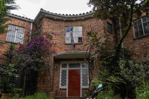 Chapinero primer plano fachada casa estilo inglés en ladrillo, rodeada de árboles y plantas altas como enredaderas.