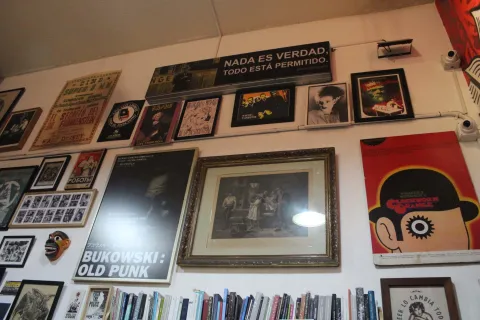 Librería La Valija de Fuego con una pared blanca repleta de cuadros de artístas y fiches de películas. También hay una repisa repleta de libros.