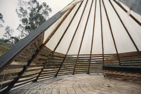 El Verjón Paramo, interior of the pyramid-shaped wooden maloka-style structure. In the background, some tall trees can be seen.