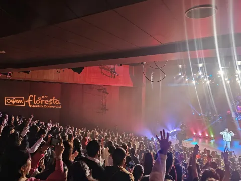 Teatro Cafam interior escenario lleno con público que levanta las manos,  con luces reflectivas y cantante en el escenario.  