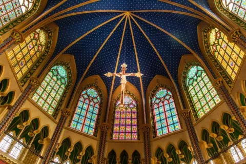 Santuario Nuestra Señora de Fátima - Tocancipá interior con vista desde abajo de la cúpula azul con estrellas, ventanales en óvalos con vitrales. Destaca al frente un Cristo crucificado que cuelga del techo. 