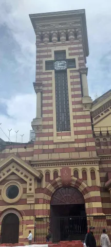Church of Our Lady of the Snows, exterior view of the tall clock tower and the blue sky with clouds. The main wooden door is open but secured with a metal gate.