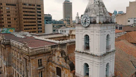 Iglesia San Francisco su blanca torre del reloj y campanario en primer plano y otros techos de edificaciones contiguas.