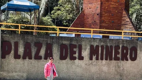 Mujer adulta piel castaño y chaqueta rosa delante del letrero Plaza del Minero. 