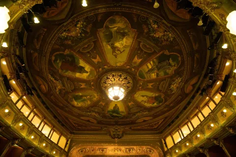 Teatro Colón, image of the dome seen from below. The paintings, the windows around the circle, and a lit lamp embedded in the very center stand out. 