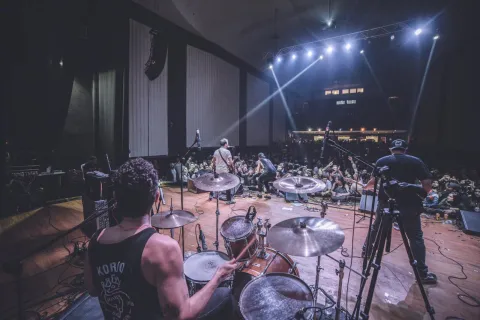  Auditorio Mayor al interior en tarima con grupo musical de rock vistos por un centenar de personas que bailan.